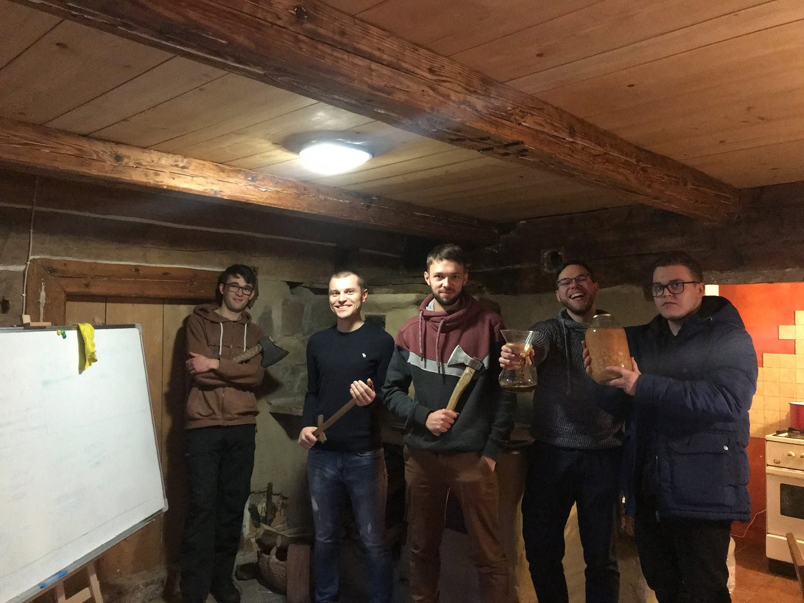 Jan Suski and colleagues in a basement workshop, holding axes and a jar of homemade infusion, celebrating.